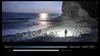 A person stands on a rocky beach at night, illuminated by a powerful flashlight beam. Produktbild-Vorschau
