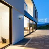 A modern house exterior at dusk, with a cat sitting near the entrance and a solar-powered wall light illuminating the facade. Podgląd zdjęcia produktu