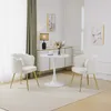 A set of two beige upholstered chairs and a small white tulip table in a well-lit room.