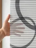 A hand is holding a piece of fabric with a striped pattern and a circular design. The fabric is semi-transparent. Produktbild-Vorschau