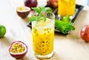 A glass of passion fruit puree with mint and ice, surrounded by passion fruits and limes on a wooden table. Podgląd zdjęcia produktu