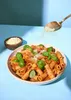 A bowl of pasta with tomato sauce and basil, with grated cheese being sprinkled on top from a spoon. Produktbild-Vorschau