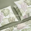 A close-up view of bedding with a tropical leaf pattern, featuring pillows and a folded sheet or duvet cover. Produktbild-Vorschau