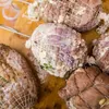 A close-up view of several raw meat rolls wrapped in netting, seasoned and prepared for cooking, resting on a wooden surface. Produktbild-Vorschau