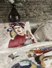 A close-up view of bedding with a Frida Kahlo-inspired print, featuring parrots and butterflies, set against a brick wall. Produktbild-Vorschau