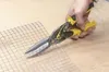 A hand is using tin snips to cut a piece of wire mesh on a wooden surface. Anteprima dell’immagine prodotto