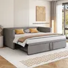 A modern bedroom with a gray sofa bed pulled out into a bed, featuring yellow accent pillows and a brown throw blanket. The room has minimalist decor, including a textured wall panel and a large window with a view of hills. Produktbild-Vorschau