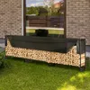 A metal firewood rack filled with wood and covered with a black tarp, placed on a lawn next to a brick building. Voir les images du produit