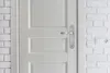A close-up of a white door with a silver door handle, next to a white brick wall with an electrical outlet. Produktbild-Vorschau