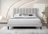 A bed with a beige upholstered headboard and frame, set in a modern bedroom with decorative wall lighting and a side table. Náhľad obrázku produktu