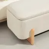 A close-up view of a cream-colored storage bench with wooden legs. Voir les images du produit