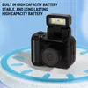 A small black digital camera with a flip-up flash sits on a speckled white surface with a blue ring. Produktbild-Vorschau