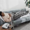 A woman is lying on a couch with her legs elevated on a special pillow and a compression device. Produktbild-Vorschau
