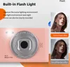 A pink digital camera with a close-up of the lens and a flash light, accompanied by two portrait images of a woman demonstrating the effect of the flash. Náhled obrázku produktu