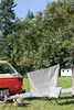 A red and beige camper van parked in a grassy area with a blanket and pillow hanging on a clothesline. Produktbild-Vorschau