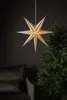 A star-shaped lantern hangs in front of a dark background, next to a Christmas tree and a sofa. Podgląd zdjęcia produktu