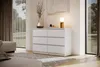 A modern white dresser with six drawers is placed in a well-lit room with large windows. Produktbild-Vorschau
