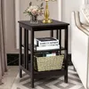 A dark brown wooden nightstand with three shelves, placed next to a sofa in a living room setting. Podgląd zdjęcia produktu
