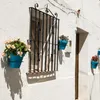 A white wall with a window and several blue flower pots with plants hanging on it. Náhľad obrázku produktu