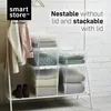 Clear plastic storage boxes stacked on a white shelf unit, with clothes hanging on the left and shoes on the bottom shelf. Produktbild-Vorschau