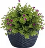 A potted artificial plant with green leaves and small purple flowers in a dark gray textured pot. Produktbild-Vorschau