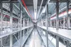 An empty warehouse aisle with rows of metal shelving and red pipes running along the ceiling. Produktbild-Vorschau