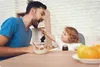 A father and child are having breakfast together. The child is feeding the father. Náhled obrázku produktu