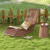A wooden lounge chair is set up on a grassy lawn next to a small wooden table, with a wooden fence in the background. Náhled obrázku produktu