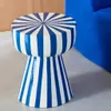 A blue and white striped stool is placed on a light gray floor next to a blue sofa. Produktbild-Vorschau