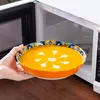 A hand holding a bowl of soup in front of an open microwave. Náhled obrázku produktu