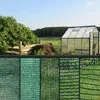A garden scene with a greenhouse and a fence made of different types of green netting. Produktbild-Vorschau