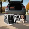 A dog is sitting next to an open dog crate in front of a car with the trunk open, suggesting travel or outdoor activity. Náhled obrázku produktu