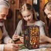A grandfather and two granddaughters are gathered around a table, looking at a detailed DIY book nook kit. Voir les images du produit