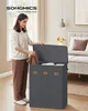 A woman is putting clothes into a gray laundry basket with three compartments. Produktbild-Vorschau