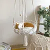 A macrame cat hammock with a stuffed cat sleeping in it, decorated with greenery and flowers on a ladder in the background. Produktbild-Vorschau