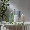 Four LED candles of different colors and sizes are arranged on a white table with ivy vines. Podgląd zdjęcia produktu
