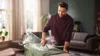A man ironing clothes on an ironing board in a living room. Voir les images du produit