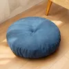 A round blue floor cushion on a wooden floor, with a hint of a white curtain and a wooden table leg in the background. Produktbild-Vorschau
