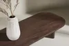 A close-up shot of a modern, dark wood coffee table with a white vase containing dried branches. Produktbild-Vorschau