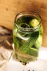 A glass jar filled with pickles and brine, placed on a white surface with a brown paper bag and a wooden background. Produktbild-Vorschau