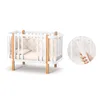A white baby crib with wooden accents, shown on a white background. Produktbild-Vorschau