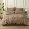 A neatly made bed with a duvet and pillows, set against a wall with decorative molding. A potted plant is visible to the left, and a bedside table with a lamp is to the right. Produktbild-Vorschau