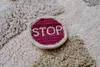A close-up of a small, round, embroidered patch with the word "STOP" on it, placed on a textured rug. Voir les images du produit
