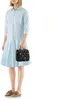 A woman stands against a white background, holding a black polka dot toiletry bag. Voir les images du produit