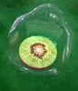 A sliced kiwi fruit is placed inside a clear, bowl-shaped object, which is resting on a green surface. Produktbild-Vorschau