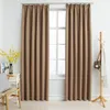 Two taupe blackout curtains are shown hanging in front of a window, with a small wooden coat rack to the right and a chair with a pillow to the left. Produktbild-Vorschau