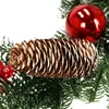A close-up view of a Christmas wreath decoration, featuring a pine cone, red berries, and evergreen branches. Náhľad obrázku produktu