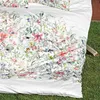 A close-up view of a white duvet cover with a colorful floral pattern, laid out on green grass. Produktbild-Vorschau