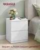 A white two-drawer nightstand next to a bed, with a vase of flowers and a candle on top. Produktbild-Vorschau