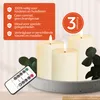 Three LED candles on a tray with a remote control and some greenery. Produktbild-Vorschau